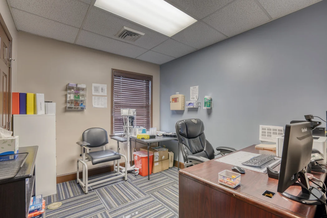 BrightView Health clinical room with patient chair, medical equipment, computer workstation, storage, and blue patterned carpet
