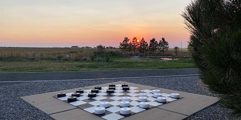 A large outdoor checkerboard set against a peaceful sunset backdrop, surrounded by open fields and trees, creating a serene and playful atmosphere.