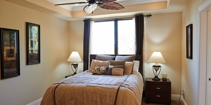 A cozy bedroom with warm lighting features a comfortable bed adorned with plush pillows, elegant decor, and a stylish ceiling fan.