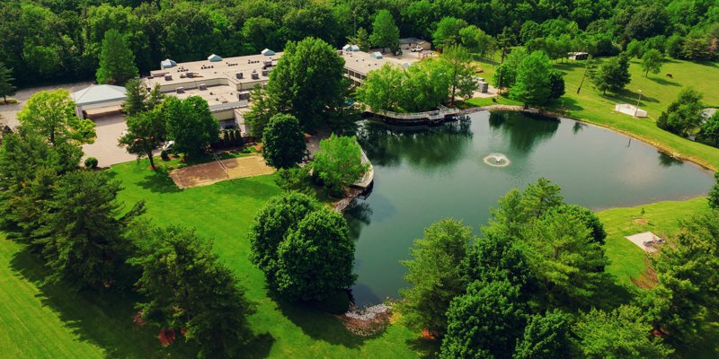 Lush aerial view of a serene facility surrounded by greenery, a peaceful pond with a fountain.