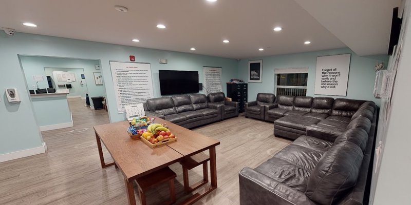  A cozy common area featuring comfortable leather seating, a large table with fresh fruit, and inspirational quotes on the walls, offering a relaxing space.