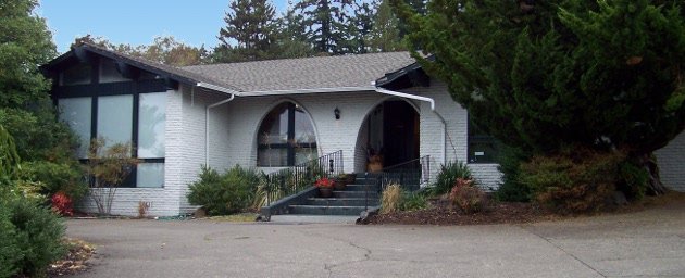 White brick house with arched entry and trees
