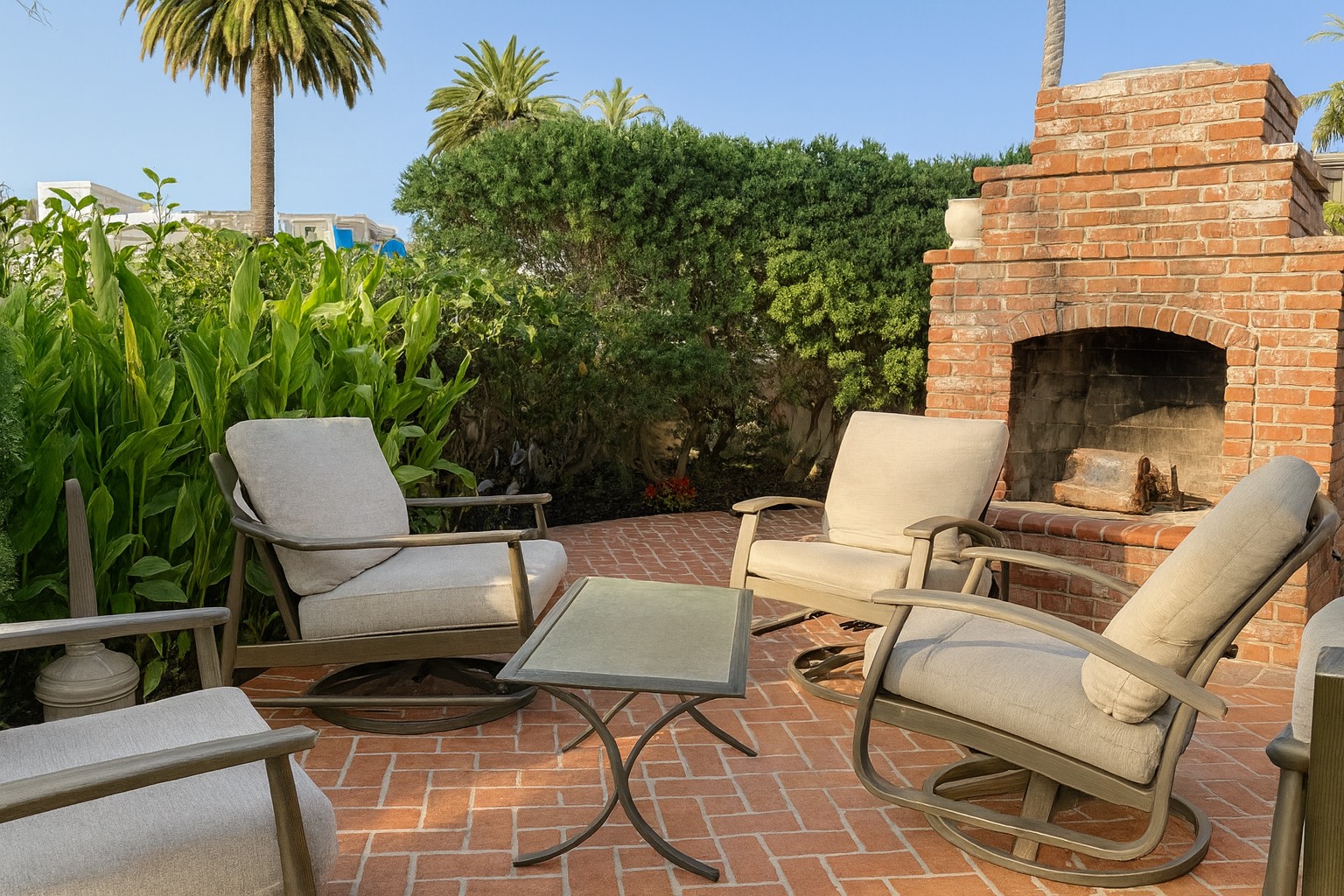 Outdoor patio with cushioned chairs surrounding a brick fireplace.