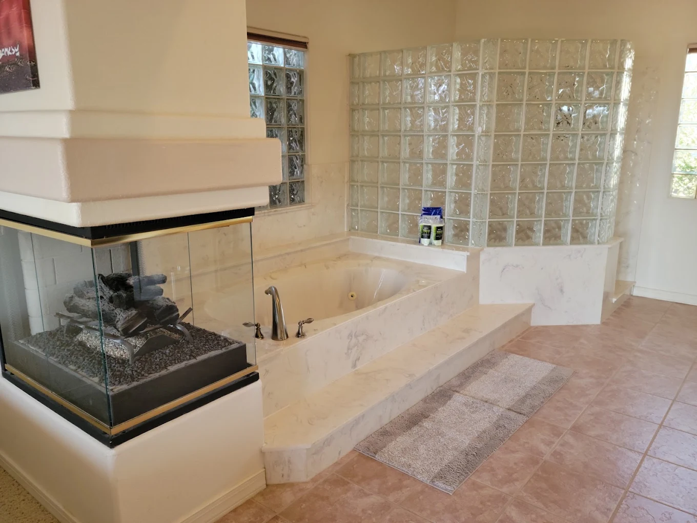 Spacious bathroom with built-in soaking tub, glass-block surround, tiled floor, and three-sided fireplace