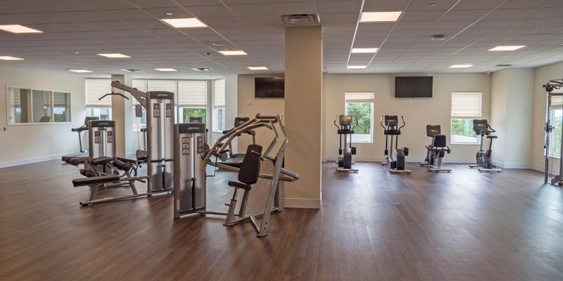 Spacious fitness center with modern exercise machines, large windows for natural light, and ample space for a comfortable workout.