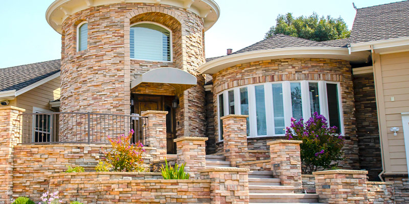 A beautifully designed home with stunning stone architecture, circular tower, and elegant landscaping, creating a welcoming and luxurious facade.