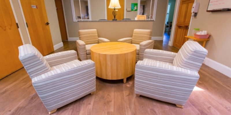 A cozy seating area with four striped armchairs arranged around a round wooden table. The space is warmly lit, with wood floors and inviting decor.