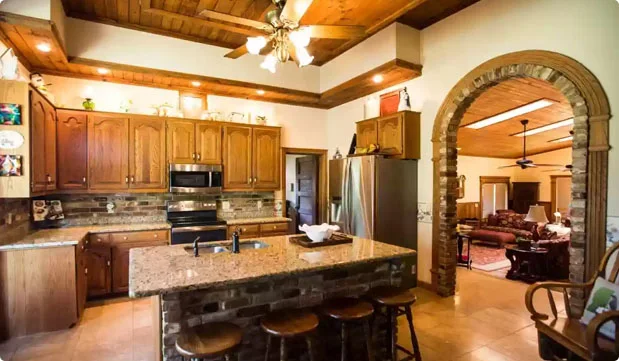 Traditional kitchen with wood cabinetry, granite island, stainless steel appliances, bar stools, and arched opening to an adjoining room