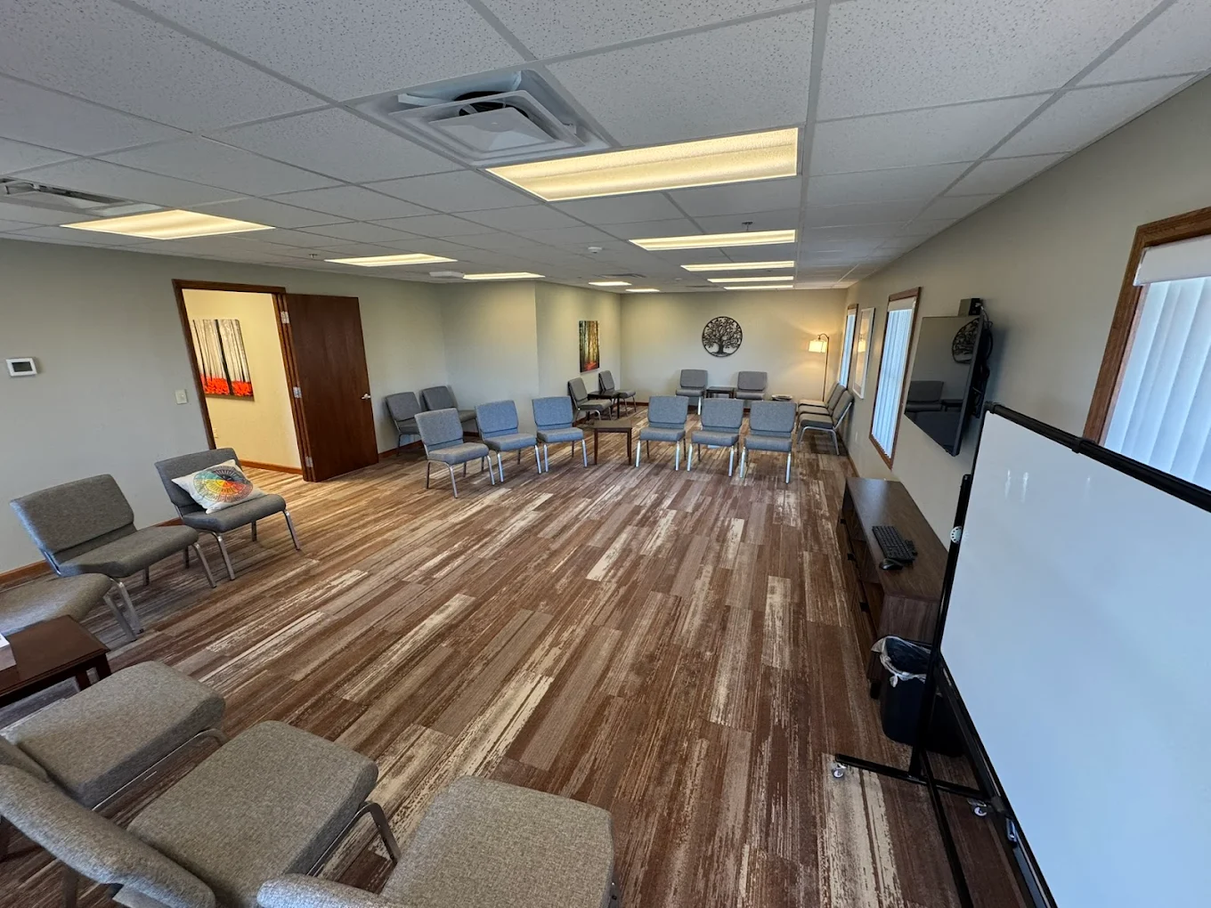 Spacious group therapy room with chairs, TV, and whiteboard