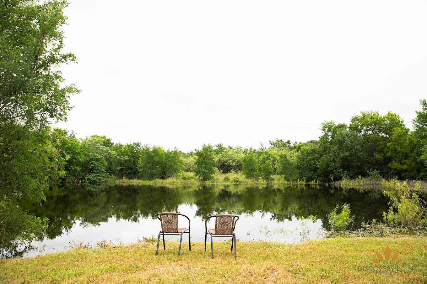 Two chairs overlooking a peaceful pond surrounded by dense green trees at Discovery Point Retreat