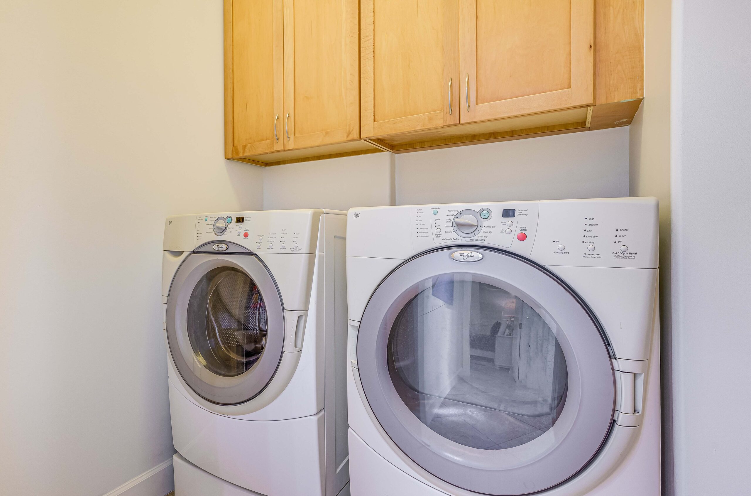 On-site laundry room with full-size washer, dryer, and storage cabinets