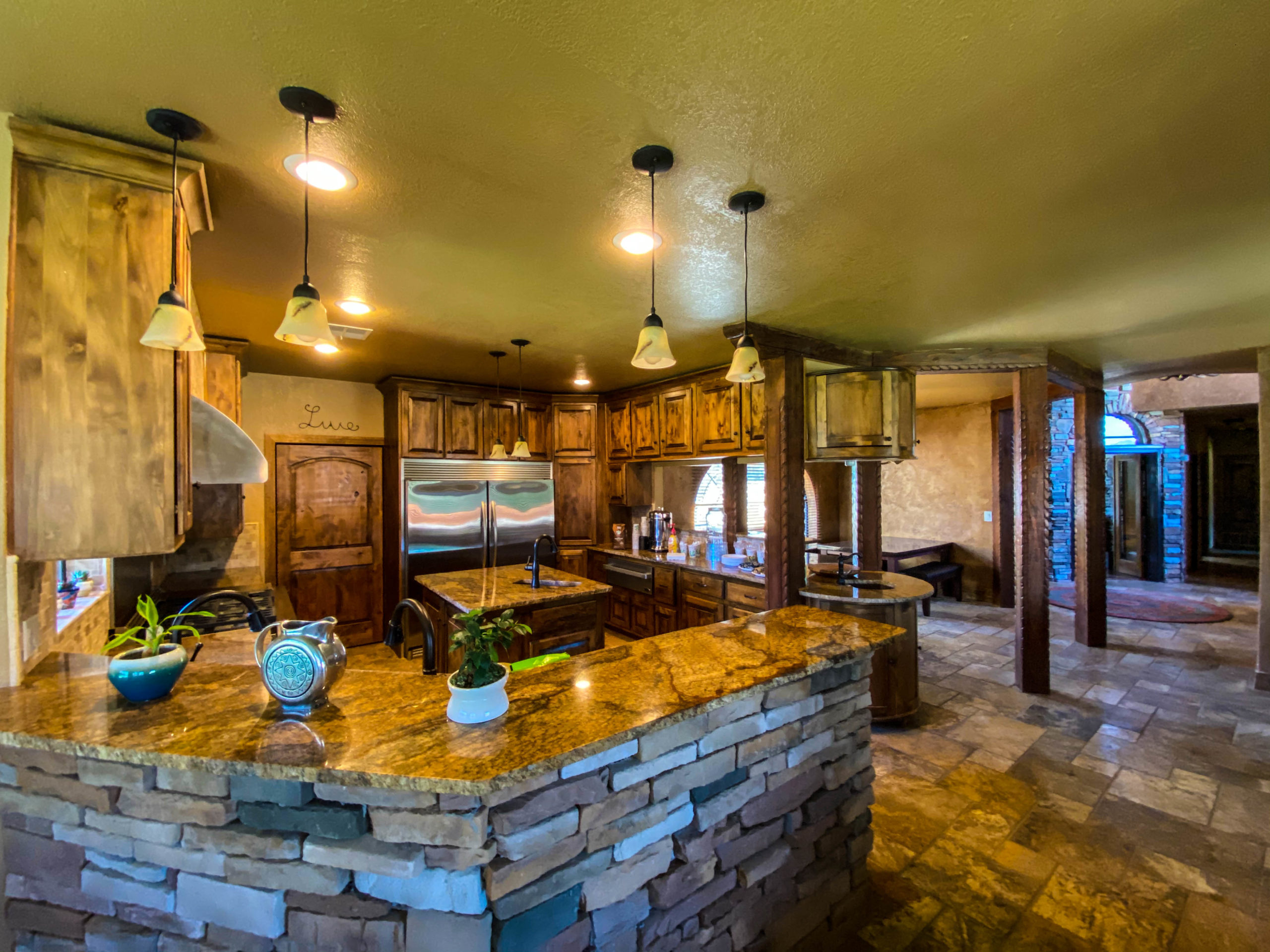 Warm-toned kitchen with stone-faced counters, wood cabinetry, pendant lighting, and stainless steel appliances