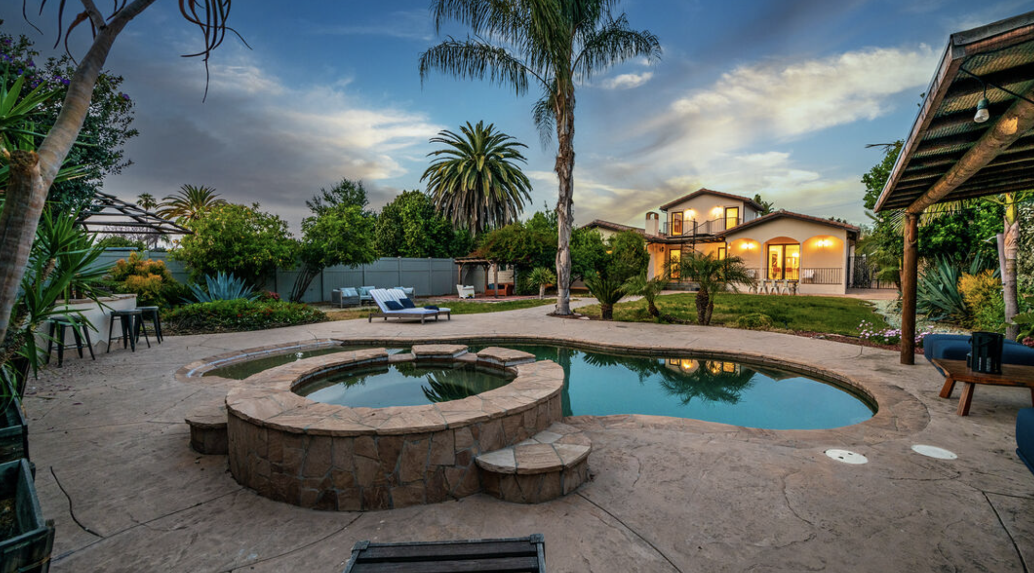 A scenic backyard with a pool, spa, and tropical landscaping.
