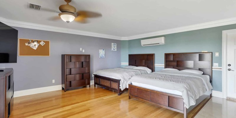 Spacious bedroom featuring two wooden beds, soft lighting, modern furnishings, and a calming color palette for a restful environment.