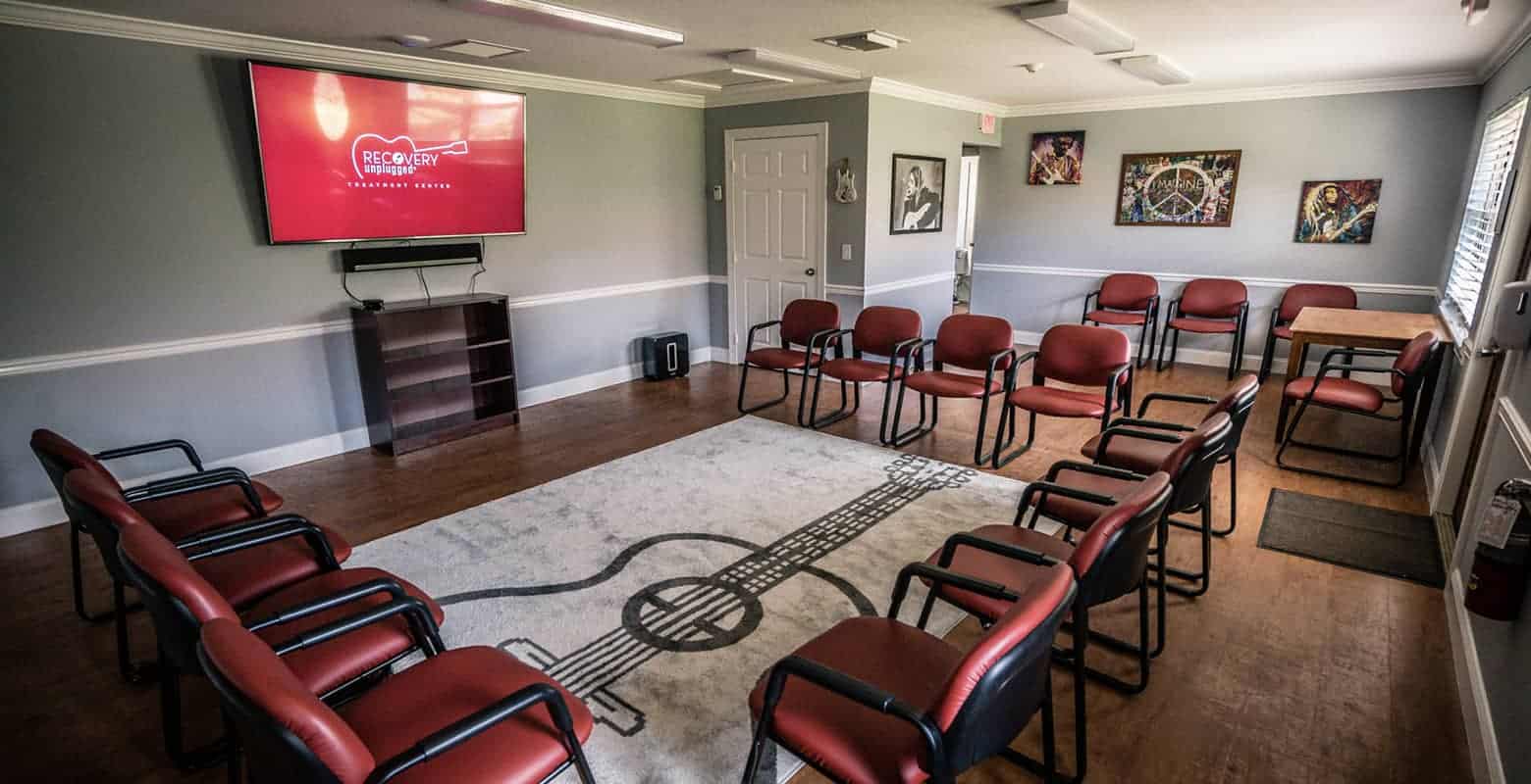 Circle of chairs in a music-themed group therapy room with a large screen.