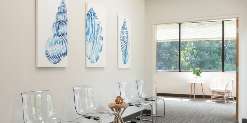 A bright, welcoming waiting area with modern transparent chairs, nature-themed artwork, and large windows offering a calming outdoor view.