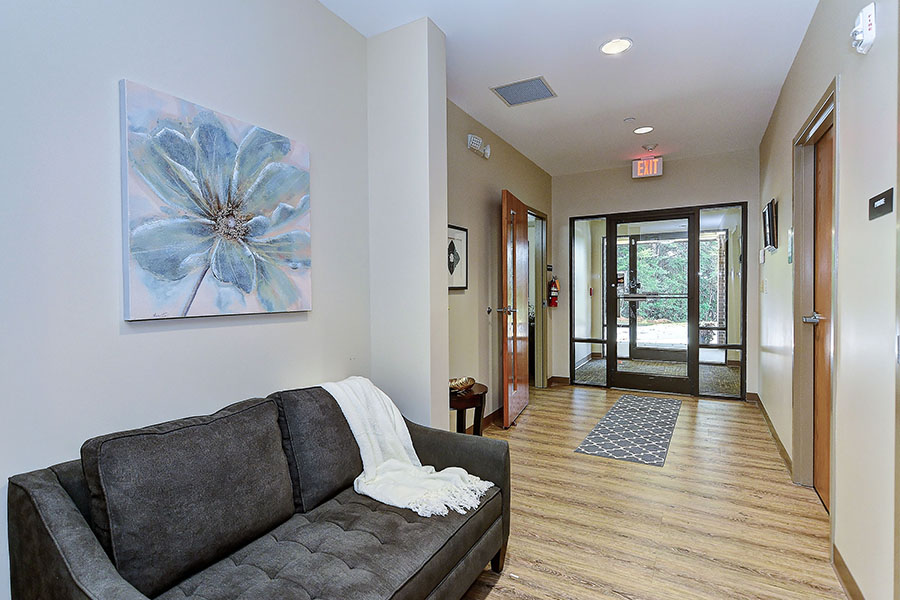 Lobby hallway with gray couch, artwork, and glass entrance door.