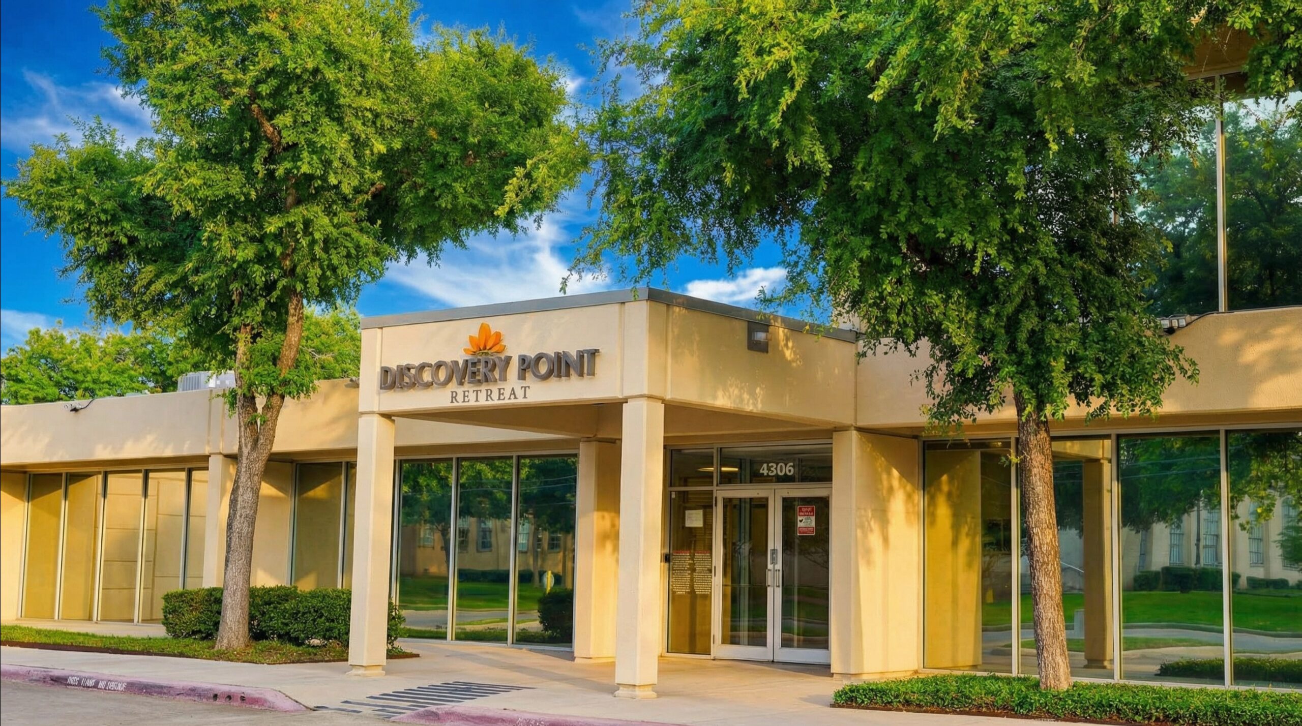 Main entrance of Discovery Point Retreat Dallas with facility signage, glass doors, large windows, and mature trees