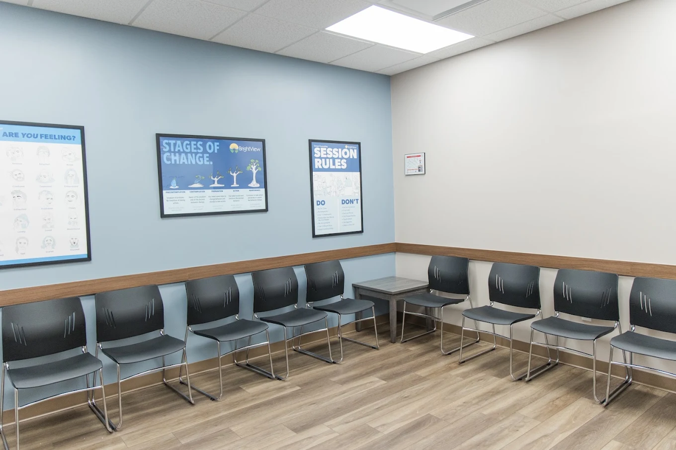 Group waiting area with black chairs arranged around the walls and educational posters about feelings, stages of change, and session rules