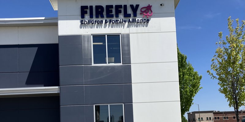 The Firefly Children & Family Alliance building features a modern design with a sleek exterior and clear signage against a bright blue sky.