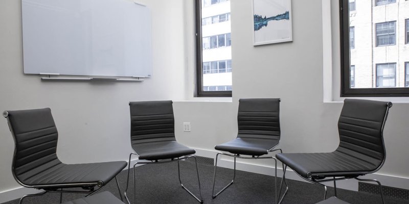 A modern meeting room with sleek black chairs arranged in a circle, a large whiteboard, and natural light from windows, creating a collaborative space.