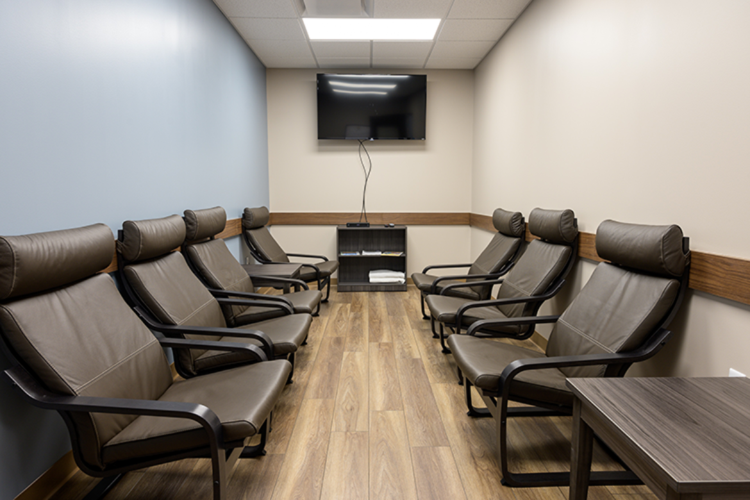Treatment room with rows of cushioned chairs, television, and wood-look flooring