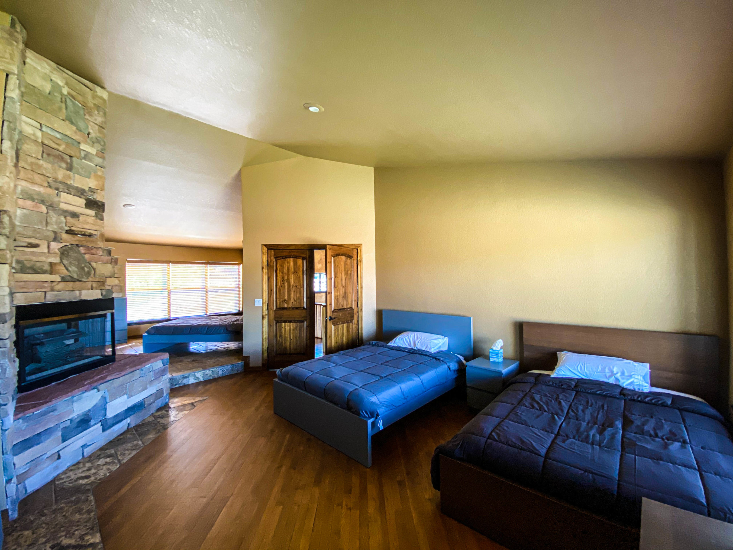 Comfortable bedroom with two beds, a fireplace, wood flooring, natural light, and stone and wood accents