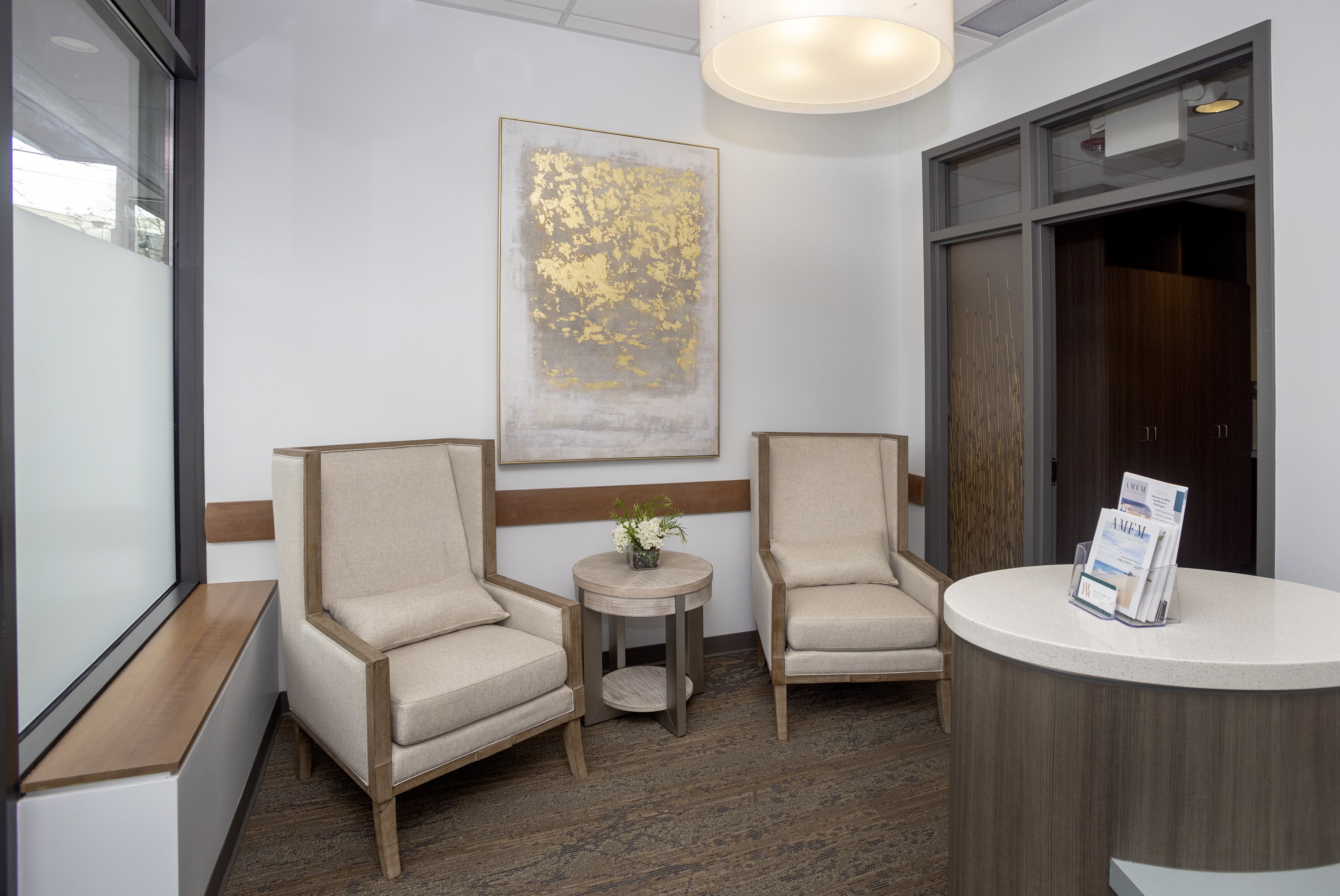 Waiting area with two beige chairs, a round table, and gold-accented artwork.