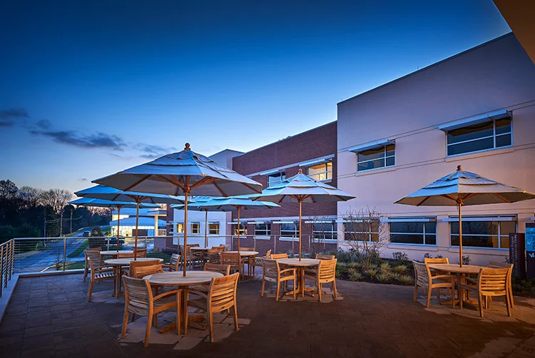 Outdoor patio at Caron Treatment Centers with wooden tables, chairs, large umbrellas, and evening lighting