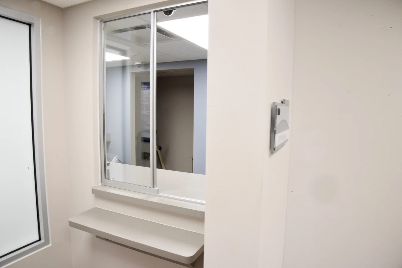 Medication dispensing area at BrightView Health featuring a secure sliding service window, counter, privacy glass, and neutral-colored walls