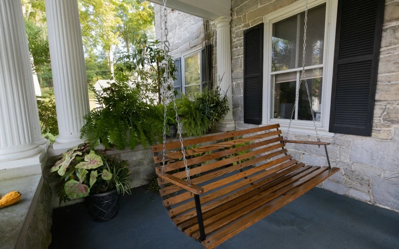 Wooden porch swing beside plants and stone walls