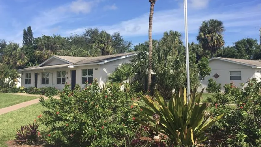 White one-story building with garden and palm trees
