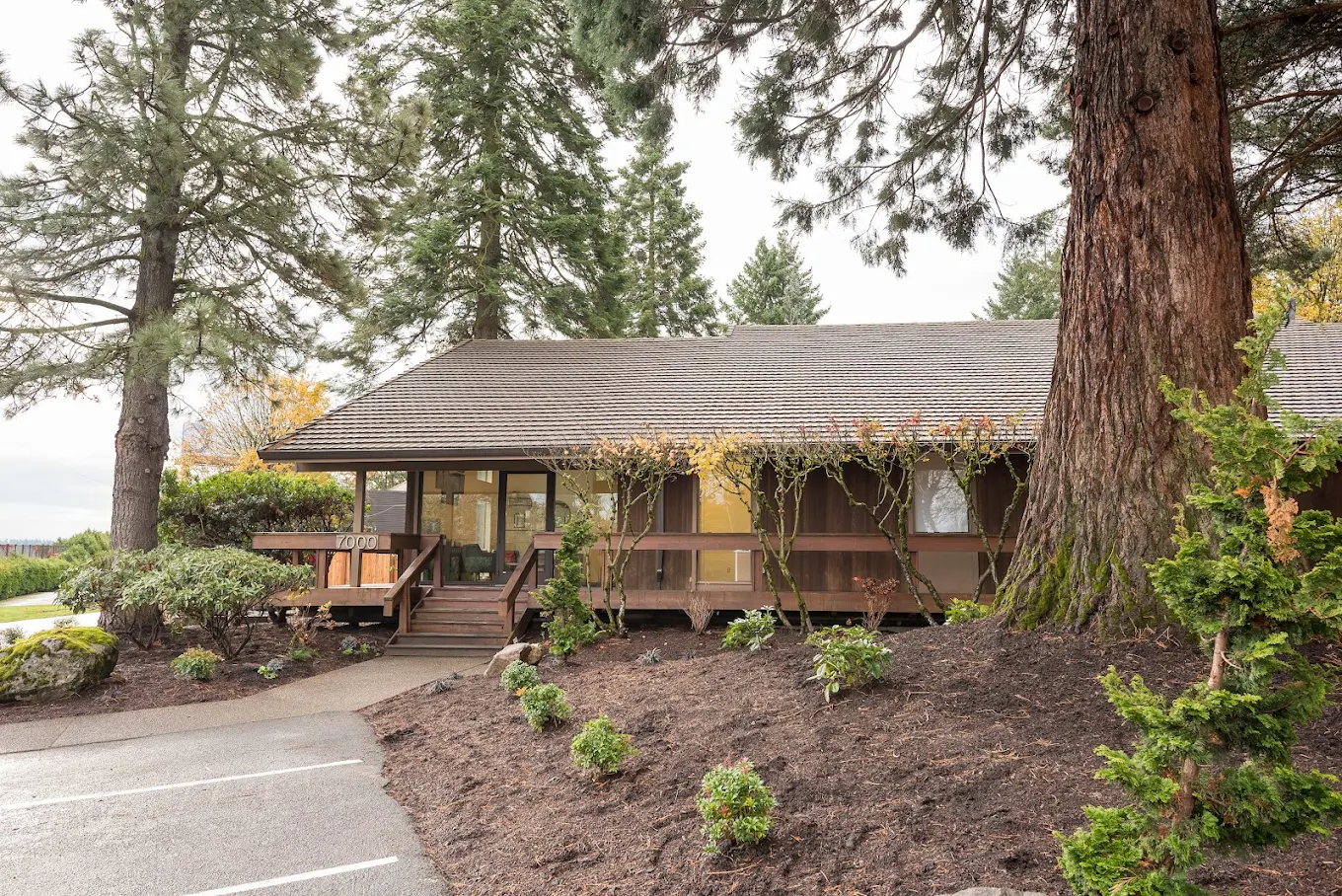 Forest-surrounded recovery center with wooden porch and natural landscaping under tall pine trees