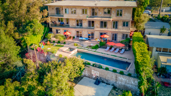 Overhead view of facility with pool, lawn, and multiple balconies surrounded by greenery