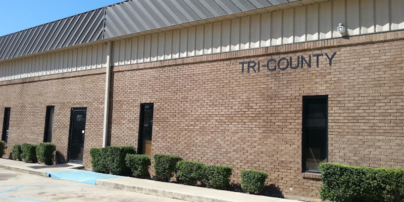 A clean, tan brick building with "Tri County" written on the facade. Neatly trimmed bushes and accessible parking are visible in front.