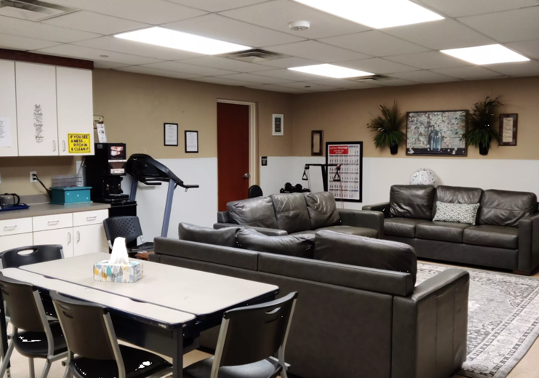 Lounge with gray sofas, kitchen area, and exercise equipment