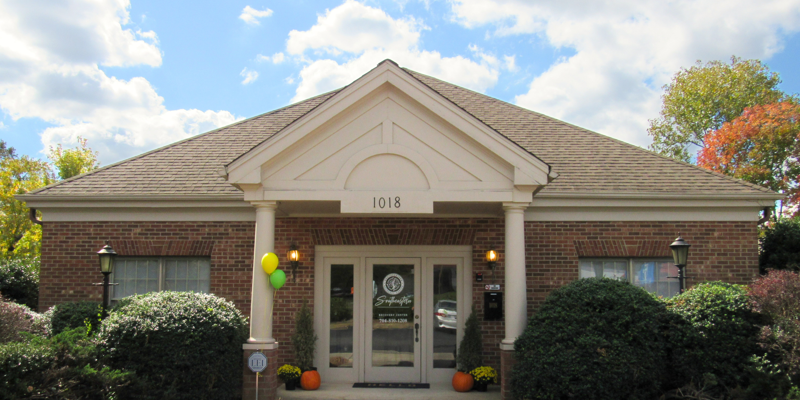 A charming brick building with a welcoming entrance, decorated with balloons and pumpkins, under a bright sky, creating a festive and inviting atmosphere.