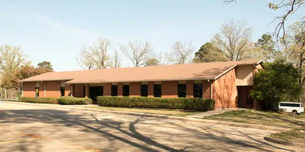 One-story brick building with trees and parking