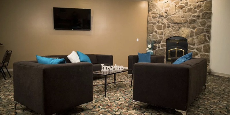  A cozy seating area with dark couches, accented by blue pillows, a stone fireplace, and a flat-screen TV, creating a relaxing ambiance.