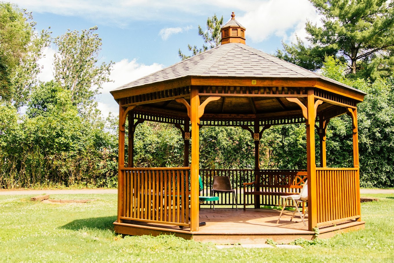 Wooden gazebo in a grassy outdoor space surrounded by trees