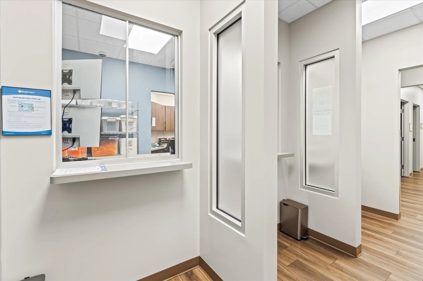 BrightView Health OTP medication dispensing area with service window, privacy panels, clinical workspace, and wood-look flooring