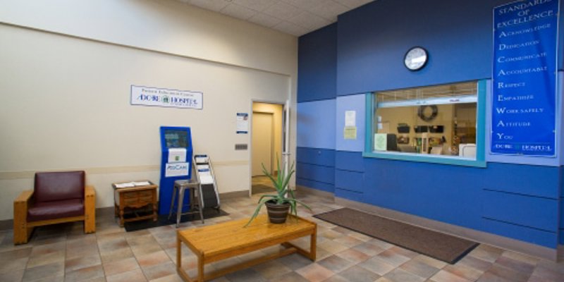 A bright lobby with a tiled floor, wooden bench, and potted plant. Blue accent wall with motivational text and a reception window adds a welcoming touch.