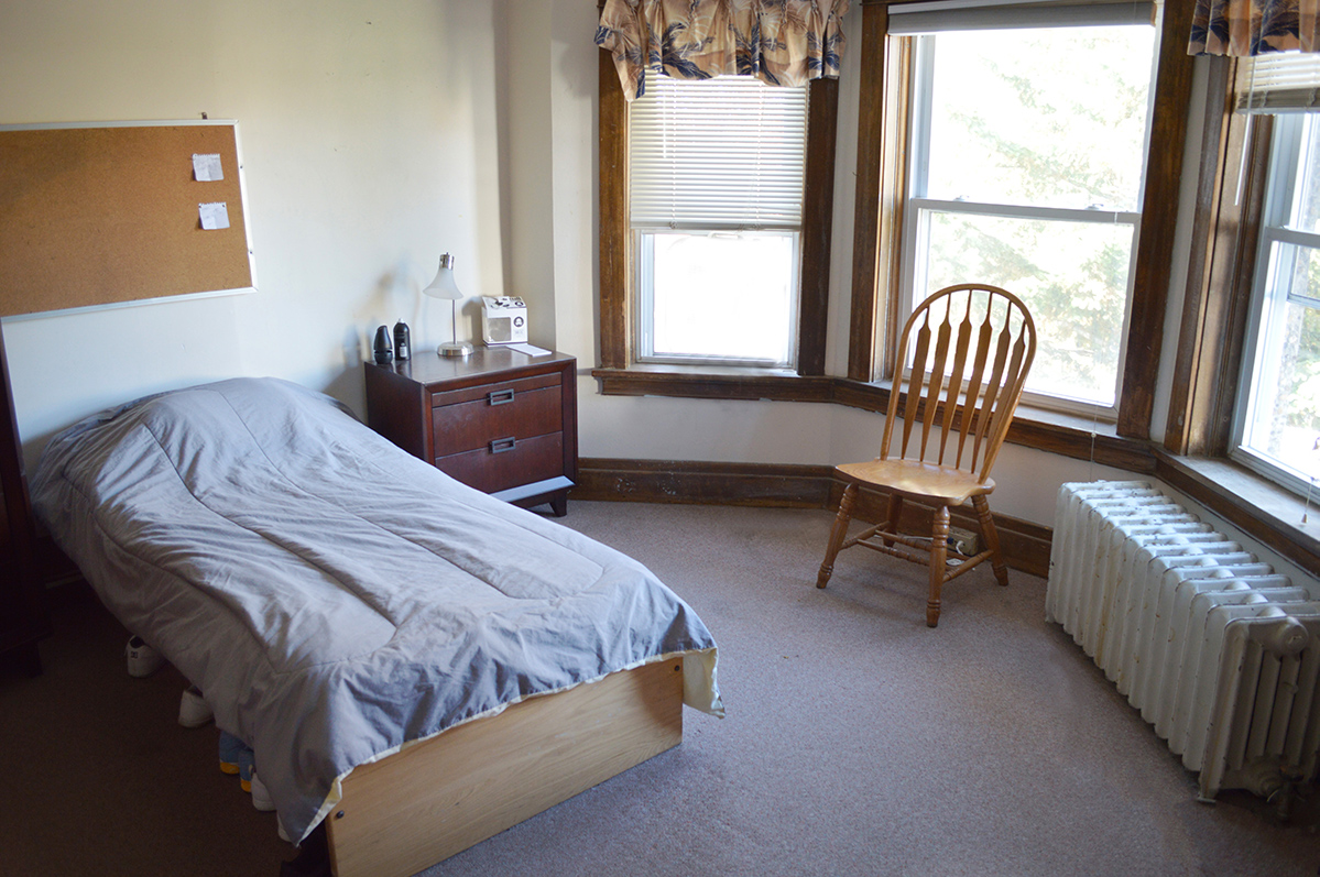 Semi-private bedroom with bed, desk, and window at Sundram Manor