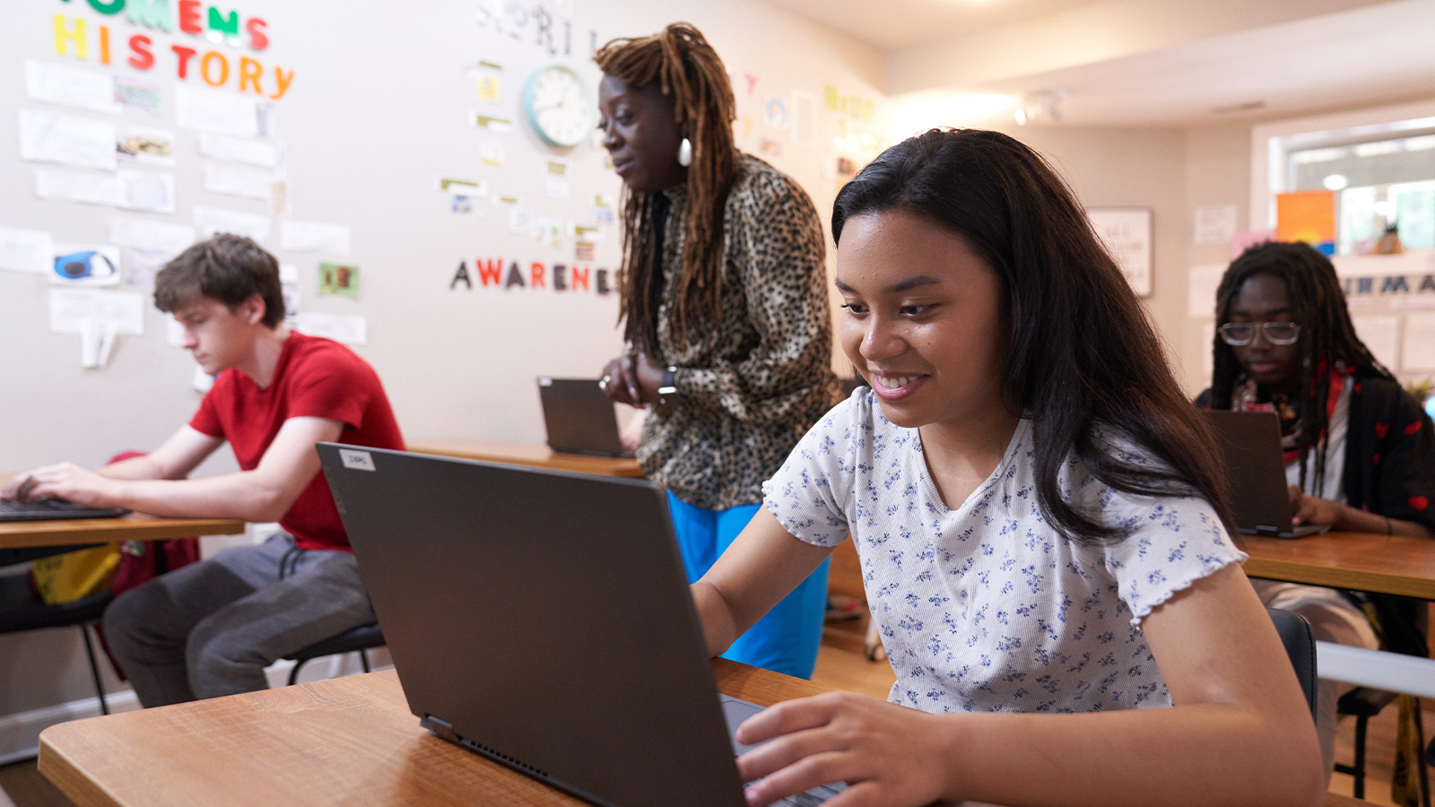 Teens working on laptops in a classroom with a teacher