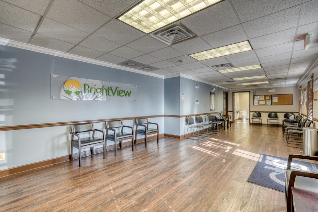 BrightView Health waiting area with rows of patient chairs, BrightView wall logo, bulletin boards, and wood-look flooring
