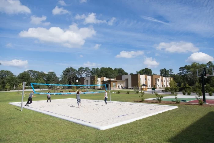 Clients playing volleyball on sand court with buildings in background