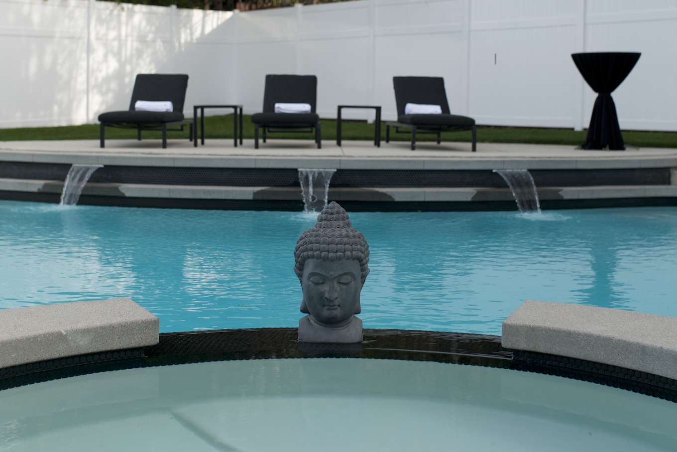 Buddha statue near pool with lounge chairs and waterfalls