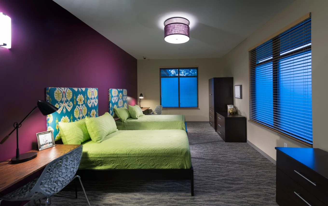 Shared bedroom with two beds, desks, and large windows