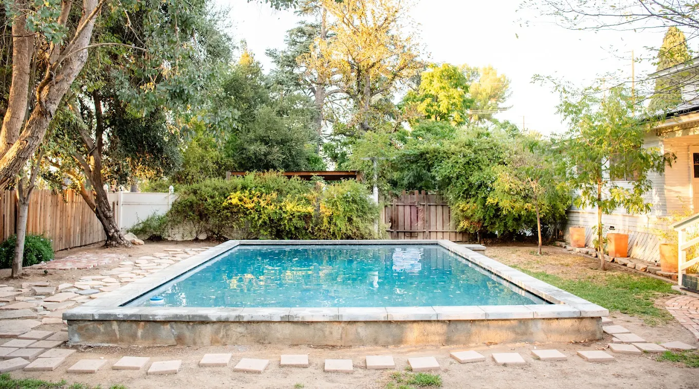 Rectangular backyard pool surrounded by trees and stone path at Liberty House Recovery