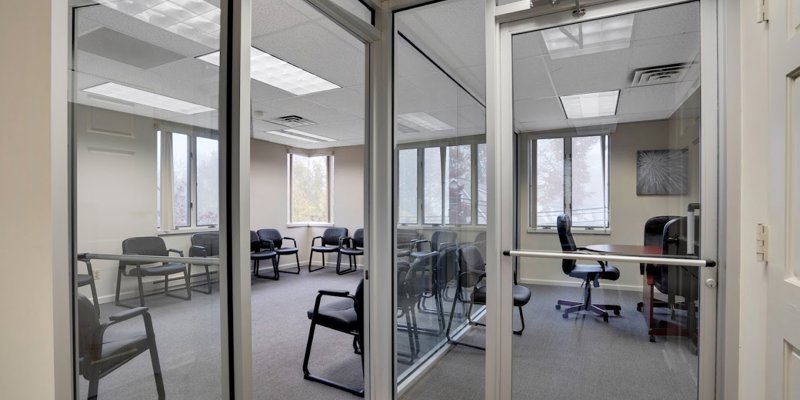 A glass-enclosed meeting room with chairs neatly arranged around tables, designed for focused group discussions and private meetings.